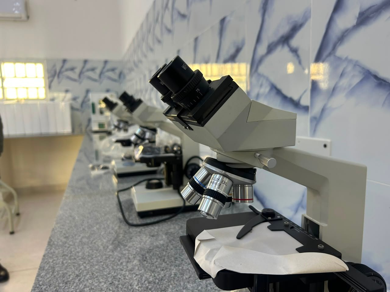 Microscópios alinhados na bancada do laboratório de análises clínicas do ISPRL